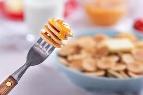 Close up tiny pancakes cereals on fork against plate of pancakes Stock Photos