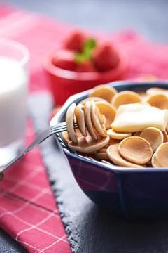 Close up tiny pancakes cereals on fork against blue bowl of pancakes Stock Photos