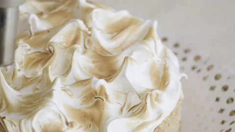Close up on tip of torch passing into the meringue topping of a cake Stock Footage 240113723