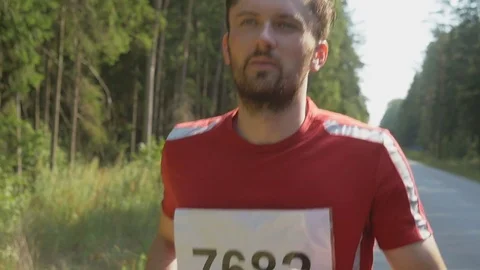Close-up of tired runner of marathon running down the road near a forest Stockbeeldmateriaal 75541194