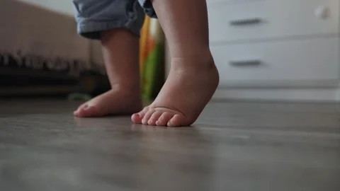 Close up of a toddler taking first steps on a wooden floor in a bright home Stock Footage 345610919