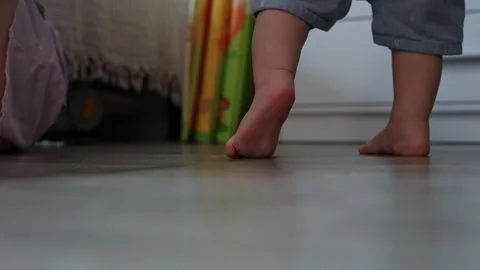Close up of a toddler taking first steps on a wooden floor in a bright home Stock Footage 345610925