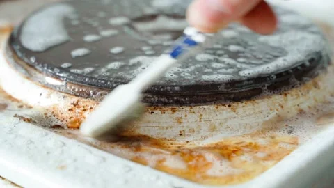 Close-up of a toothbrush rubbing an old dirty electric stove in detergent close Stock Footage 201611546