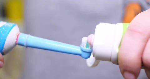 A close-up of toothpaste is applied to an electric toothbrush. Hands squeeze Stock Footage 234560219