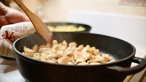 Close-up top-down: Chicken meat sizzling in black skillet, stirred Stock Footage 311753394
