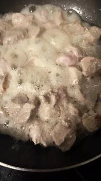 A close-up, top-down view of diced meat cooking in a dark frying pan. Stock Photos