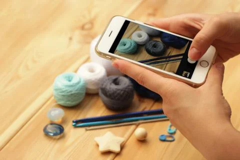 A close-up on top is a table with crochet hooks and yarn balls. Young woman h Stock Photos