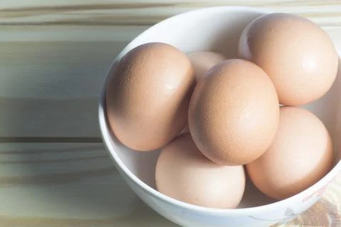 Close up top view raw chicken eggs in a white bowl on wooden table. Stock Photos