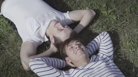 Close-up top view of relaxed young men lying on green summer grass with closed Stock Footage 145809634