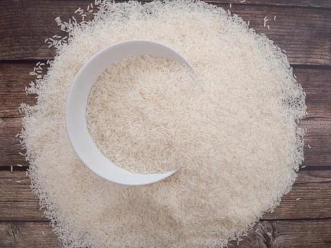 Close up top view rice in a white bowl and scattered near on wooden table wit Stock Photos