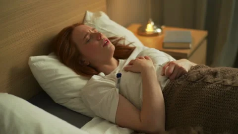 Close-up top view of sick young woman coughing heavily lying in bed at home or Stock Footage 155118061