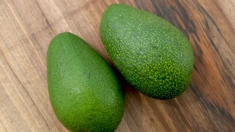 Close-up Top view of two whole avocado fruits rotating on a wooden surface Stock Footage 272222783