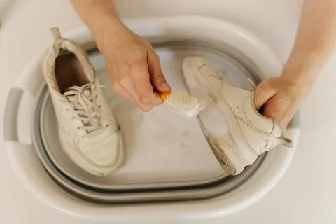 Close-up top view of unrecognizable man cleaning white sneaker with brush and Stock Photos
