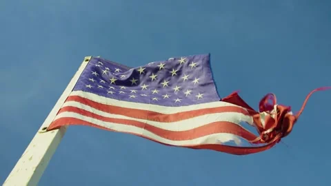 Close-up of a torn American flag fluttering in the wind against blue sky. Stock Footage 321344743