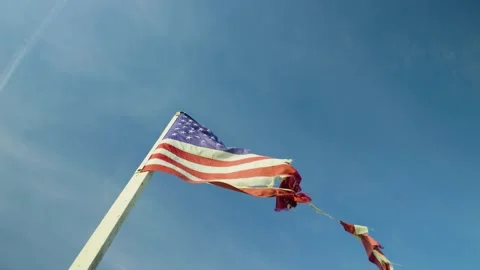 Close-up of a torn American flag fluttering in the wind against blue sky. Stock Footage 321344783