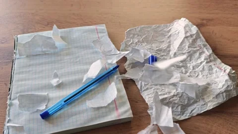 Close-up of torn paper pieces, a checkered notebook with a blue pen, and a crump Stock Footage 347964905