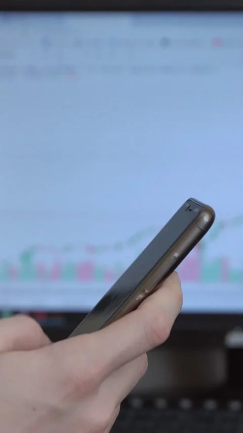 Close up of a traders hand scrolling on a smartphone with a blurred stock market Stock Footage 341679354