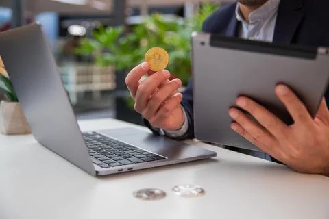 Close-up of a trader's hands holding a bitcoin coin while monitoring the mark Stock Photos