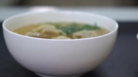 Close-up of traditional meat dumpling soup garnished with fresh herbs in a white Stock Footage 342345275