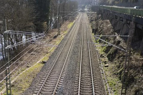 A close-up train tracks with power lines next to a stone wall. Railway transp Stock Photos