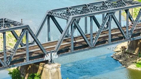Close up of train tracks on truss train bridge over flowing river with rippled Stockfoto's