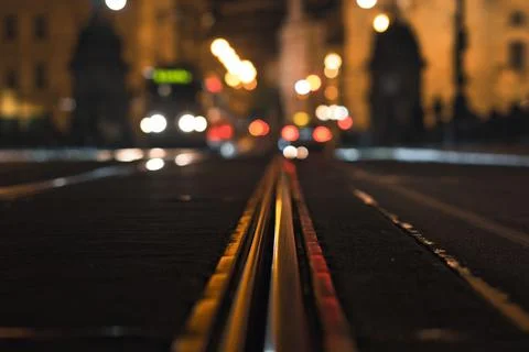 Close-up of tram tracks in a city at night with blurred lights and buildings in Fotos de archivo