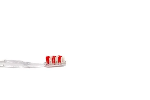 Close-up of a translucent toothbrush with red and white bristles on a white.. Stock Photos