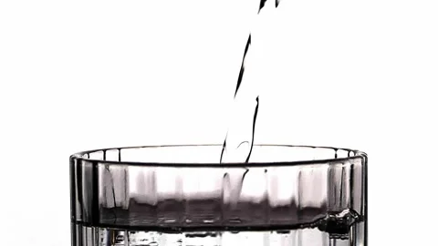 A close-up of a translucent water glass filled with bubbles and water splashes. Stock Footage 228764939