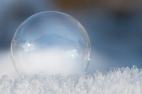 Close-up of a transparent and glowing soap bubble lying on glittering snow... Stock Photos