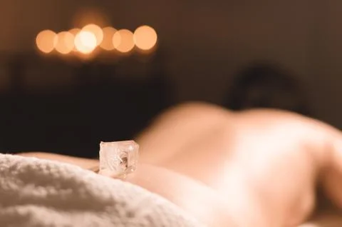 Close-up of a transparent ice cube lying on the lower back of a young girl lying Stock Photos