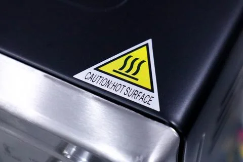 Close up of a triangular sticker with caution hot surface text and a yellow.. Stock Photos