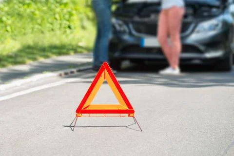 Close-up Of A Triangular Warning Sign With Couple Standing In Front Of Broken Foto stock