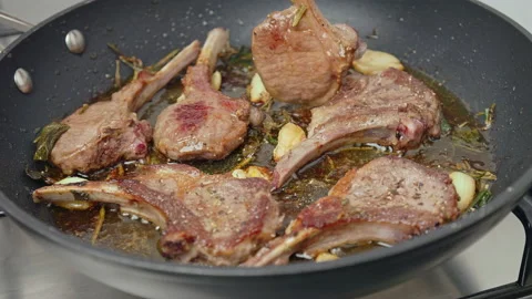 Close-up turning on the other side lamb ribs cutlets in a frying pan with greens Stock Footage 146000264