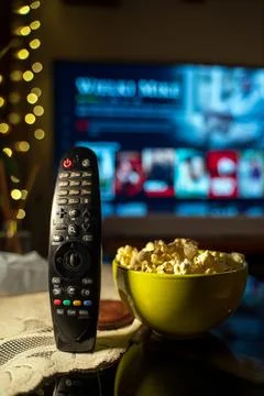 A close-up of a TV remote control on a table with a bowl of popcorn in the .. Stock Photos