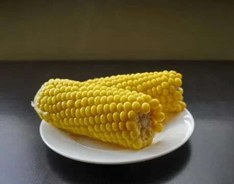 Close-up of two boiled corn cobs on a white plate with steam rising, fresh .. Stock Photos