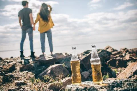 Close-up two bottles of beer stand on stones near the water in the sun on a Stock Photos
