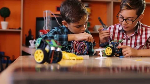 Close up of two boys assembling robots with screwdrivers on the table in the Stock Footage 82488391