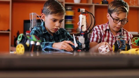 Close up of two boys mastering and playing with a small robotic machine on the Stock Footage 82487346