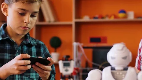 Close up of two boys operating and making a small robot walk on the table with Stock Footage 82486333