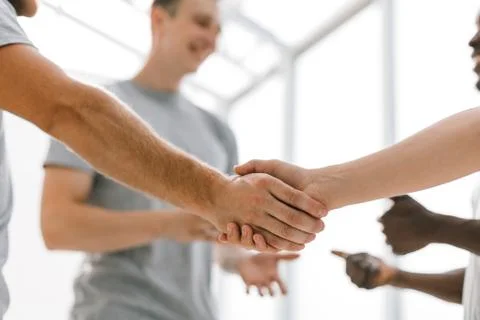 Close up. two comrades shaking hands, standing in a circle of friends Stock Photos