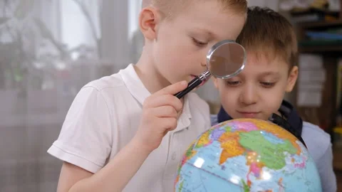 Close-up two cute little boys look at the globe through a magnifying glass. Stock Footage 328025192