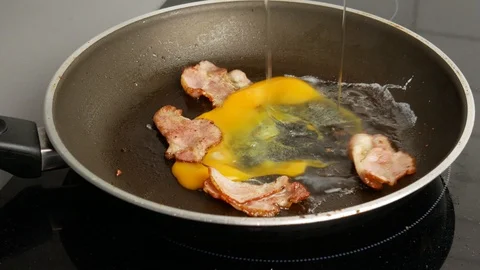 Close up. Two eggs break into a hot frying pan with fried bacon. Breakfast and Stock Footage 107393667