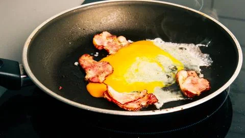 Close up. Two eggs break into a hot frying pan with fried bacon. Breakfast and Stock Photos