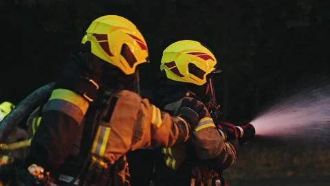 Close up, two firefighters extinguish fire, spraying with hose at night. Stock Footage 143514639