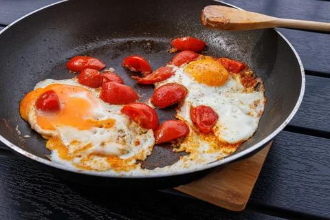 Close up of two fried eggs cooked with cherry tomatoes in a frying pan on a.. Фото