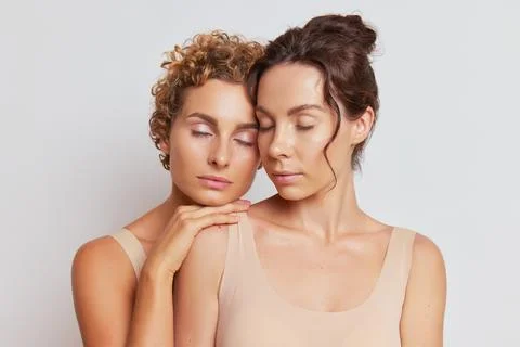 Close up of two girlfriends hugging each other standing on white background with Stock Photos