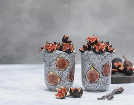 Close up two glasses of chia pudding decorated with fresh baby figs with spoon Stock Photos