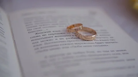 Close-up two gold wedding rings lie on page of the book with speaking text Stock Footage 100686493