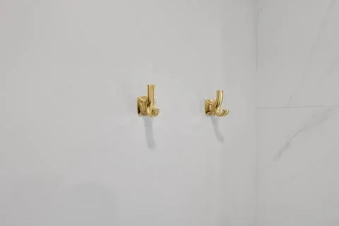 Close-up of two golden hooks mounted on a white wall, adding a touch of luxur Stock-Fotos
