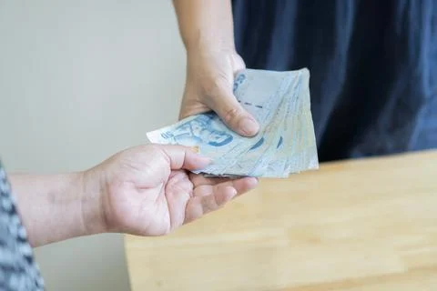 Close up of two hands taking and giving Thai bank notes. Hand receiving mon.. Stock Photos